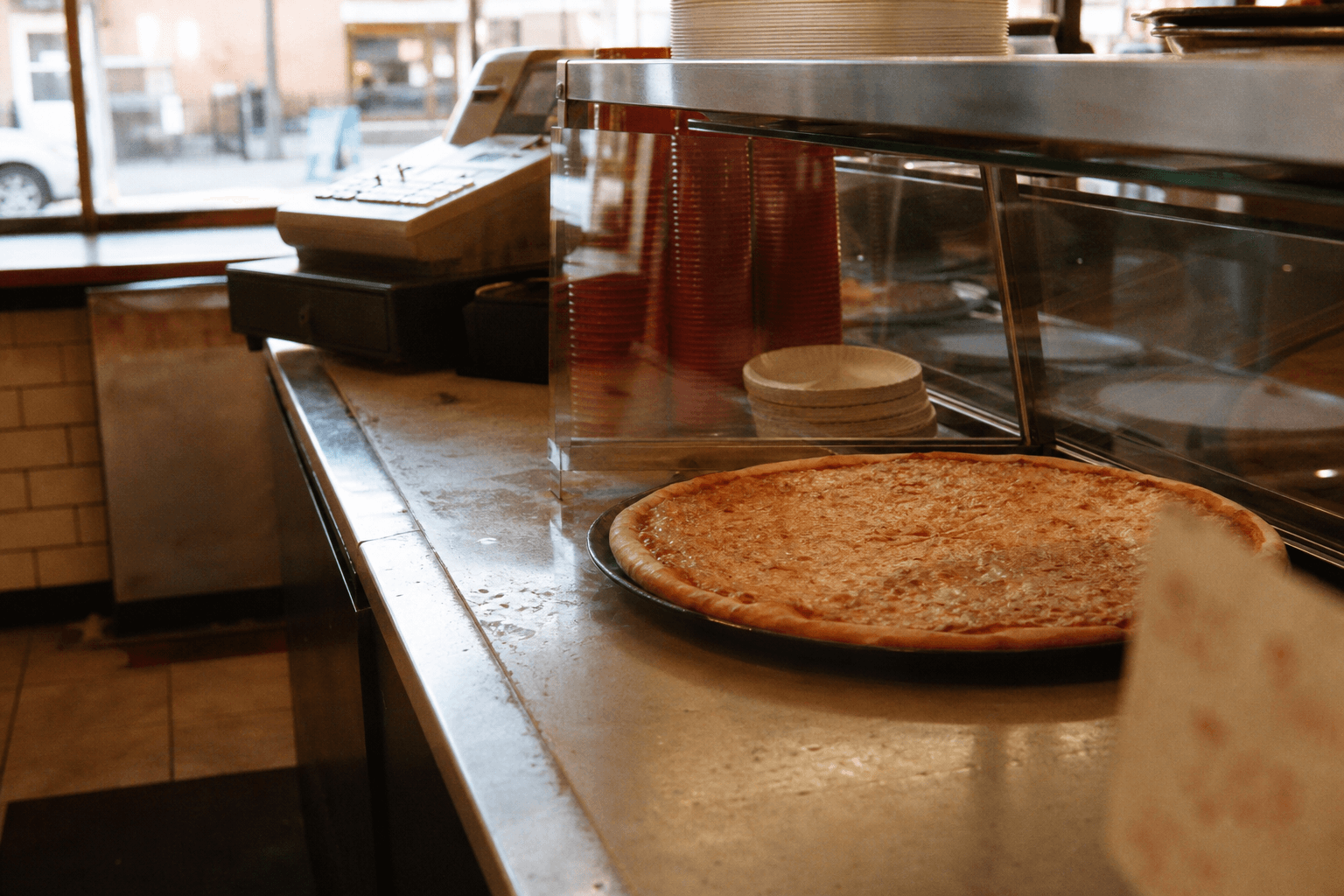 The counter of a small independent pizzeria, a cheese pie under glass
